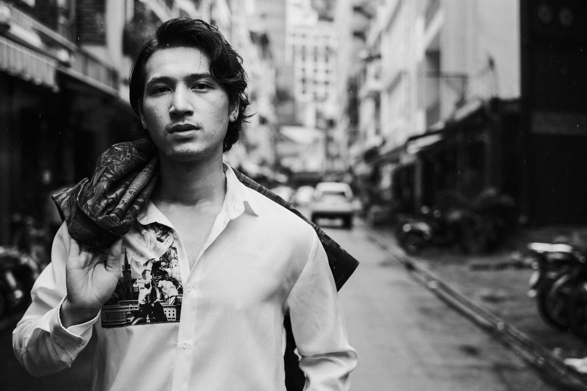 confident young ethnic man with blazer over shoulder standing on street