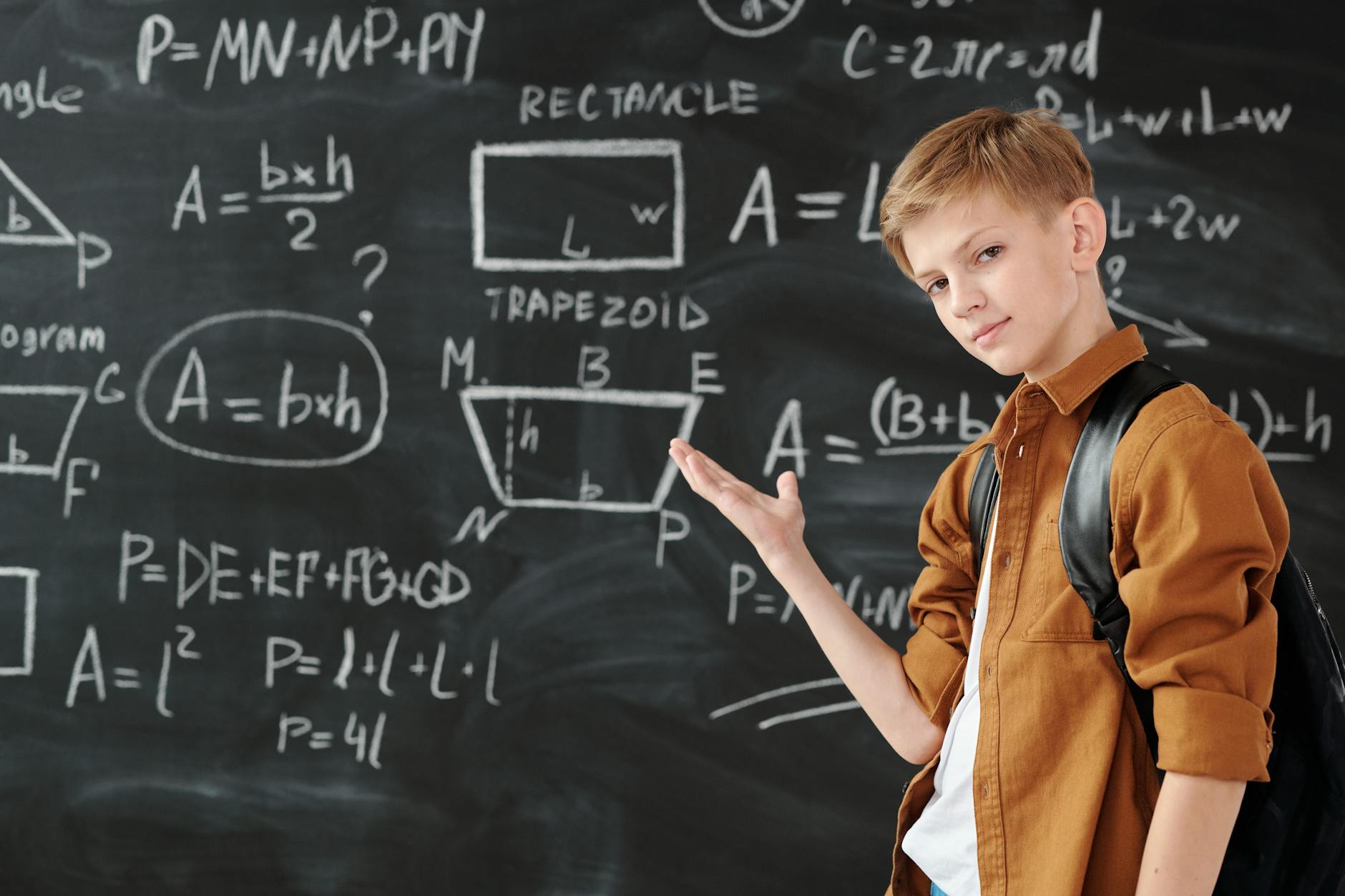 boy in brown jacket standing in front of chalk board